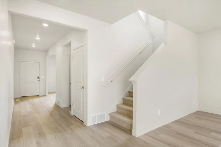 Light wood-finish flooring, recessed lighting, white interior doors, staircase with carpeted treads, and a white handrail