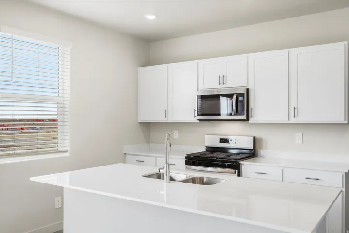Kitchen featuring white cabinetry, stainless steel appliances, a center island with a double basin sink, and solid surface countertops