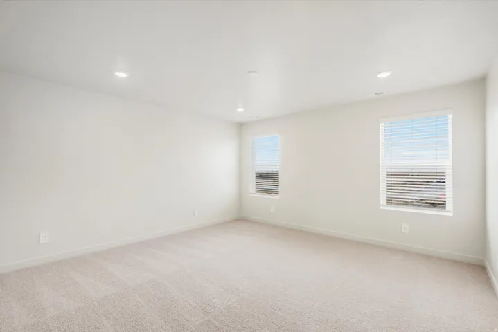Recessed ceiling lighting, light-toned carpeting, neutral wall color, and two windows with horizontal blinds