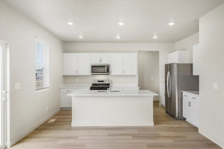 Modern kitchen featuring a central island, white cabinetry, stainless steel appliances, and wood-finish flooring
