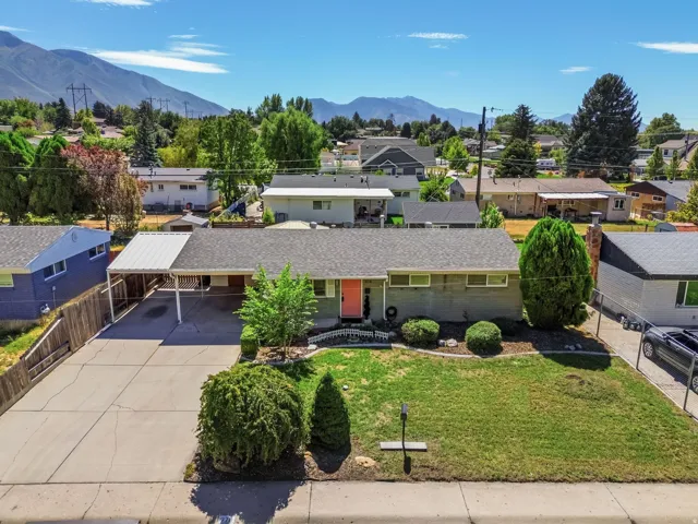 Single-story residence featuring a covered carport, mature front yard landscaping, paved driveway, and a shingled roof