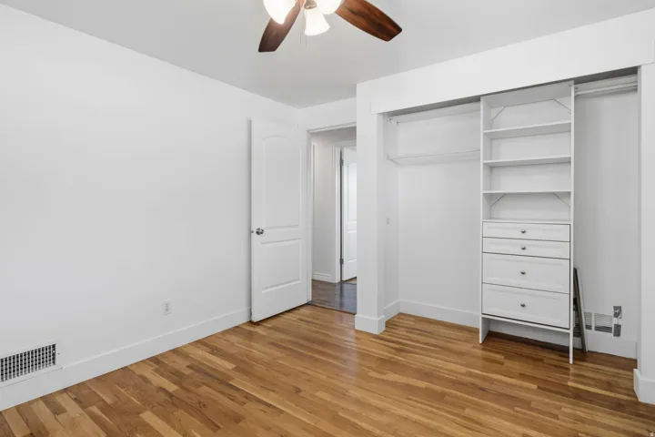 Hardwood flooring, ceiling fan, white paneled door, built-in closet shelving, and built-in closet drawers
