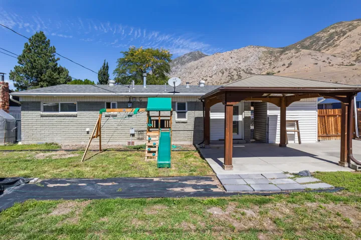 Expansive backyard featuring a covered patio, mountain backdrop, and a brick exterior