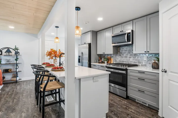 Kitchen featuring light gray cabinetry, stainless steel appliances, a white countertop island, and wood-finish flooring