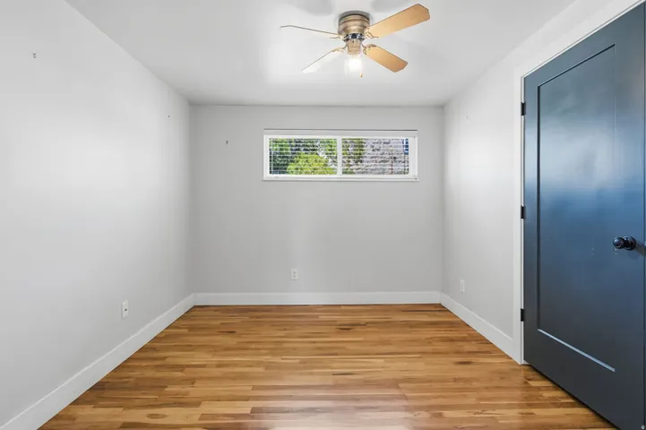 Wood-finish flooring, neutral wall tones, a ceiling fan with light fixture, and a window with blinds