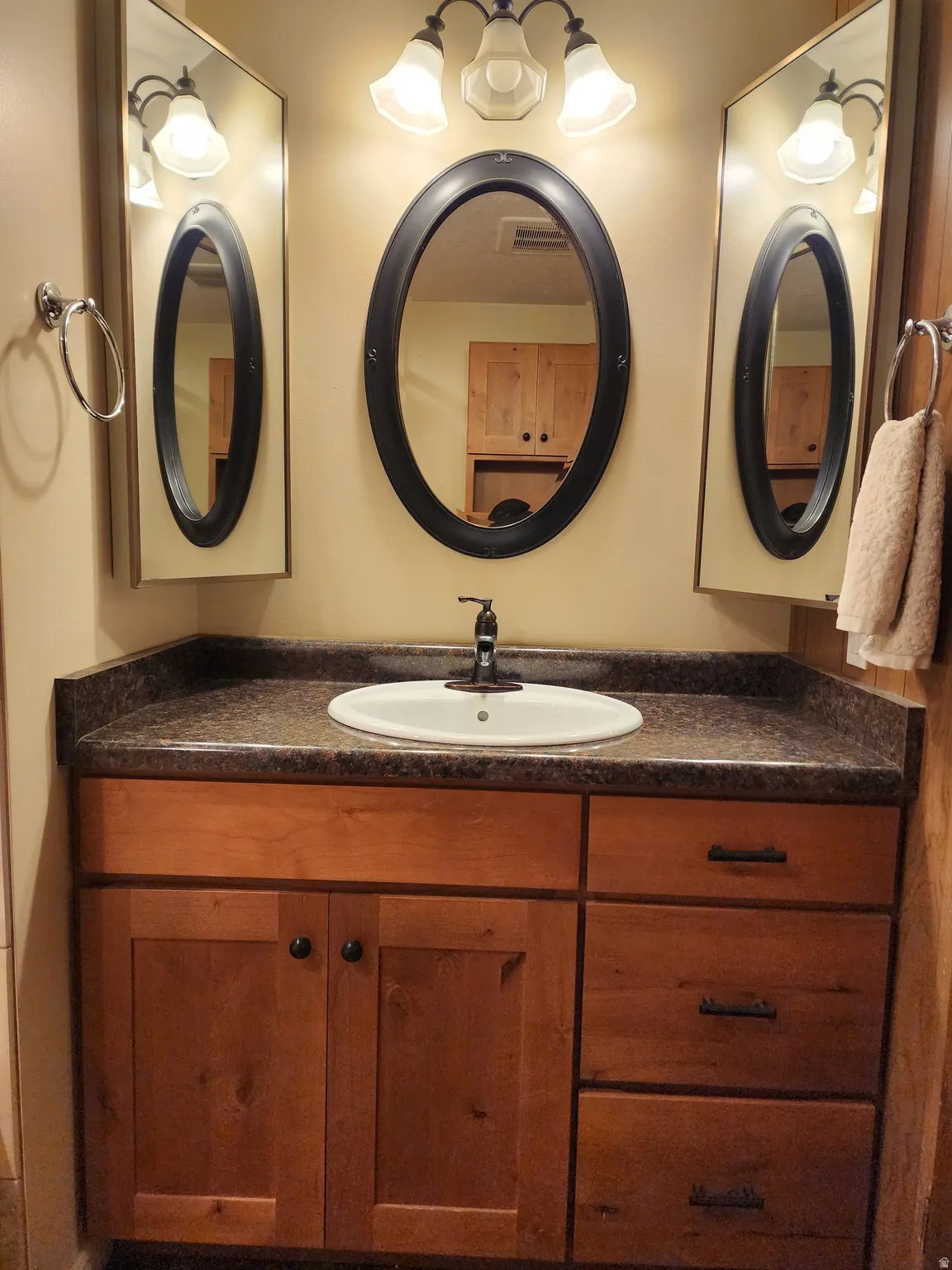 Vanity with wood-finish cabinetry, integrated sink, and dark countertop