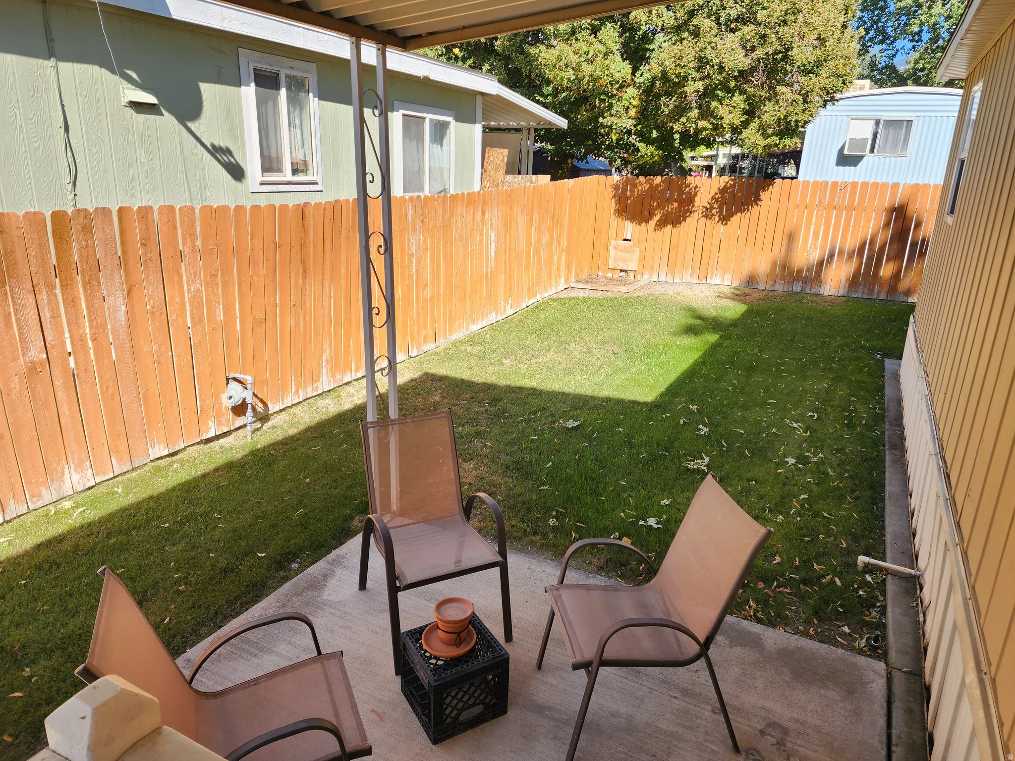 Covered patio with a concrete surface, leading to a fenced yard with a grass lawn