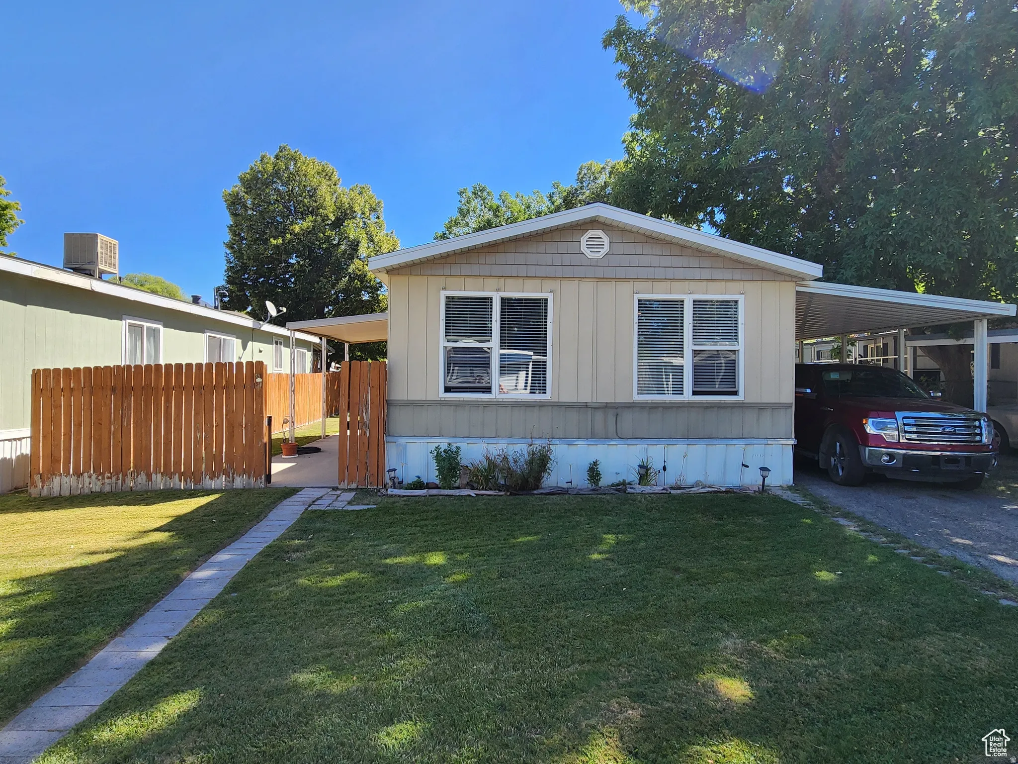 Single-story residence featuring light-colored siding, a covered carport, and a wooden privacy fence