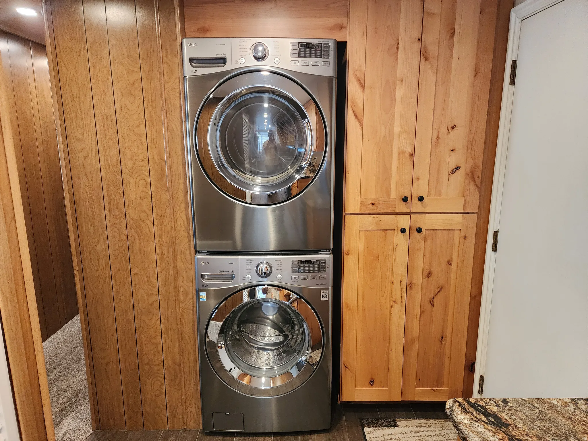 Stackable laundry appliances, wood paneling, and built-in wood cabinetry with dark hardware