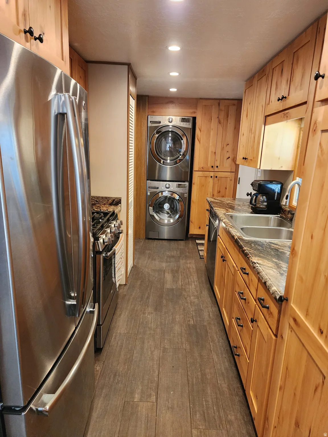 Galley kitchen featuring stainless steel appliances, wood-finish flooring, recessed lighting, and custom wood cabinetry with dark hardware