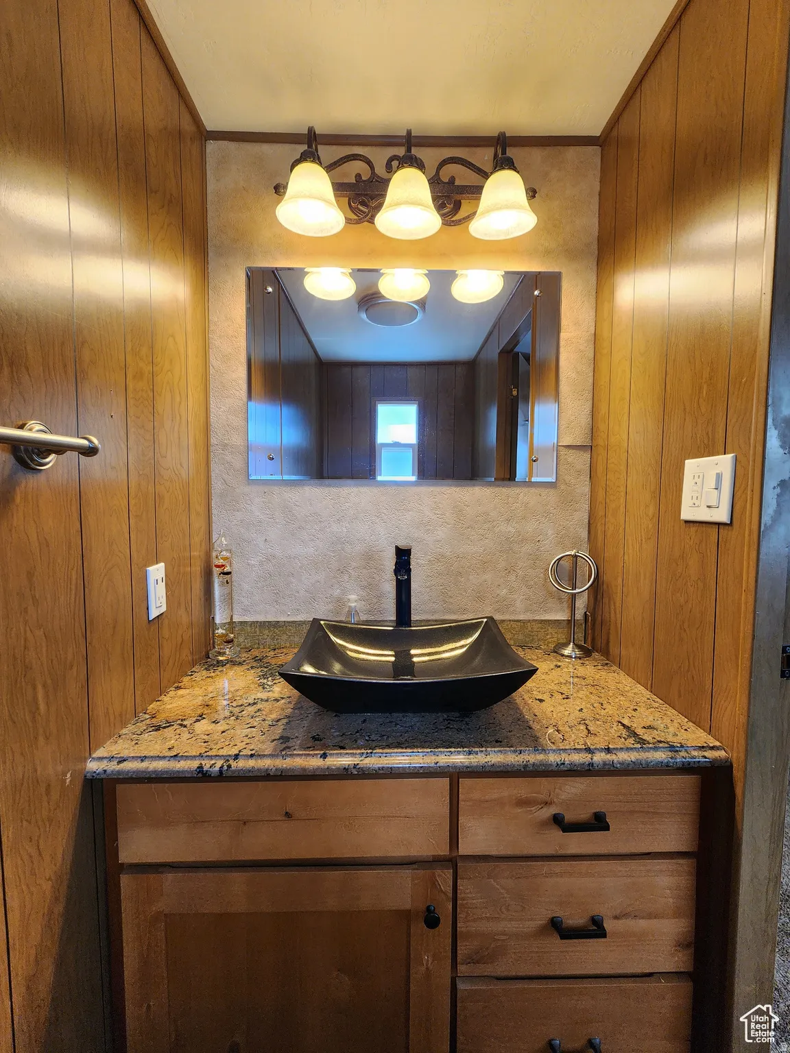 Wood paneling walls, vanity with a vessel sink, dark finish faucet, granite-style countertop, and wood-finish cabinetry