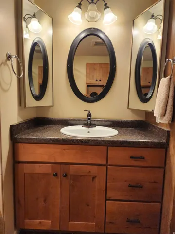 Vanity with wood-finish cabinetry, integrated sink, and dark countertop