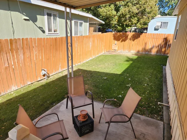 Covered patio with a concrete surface, leading to a fenced yard with a grass lawn