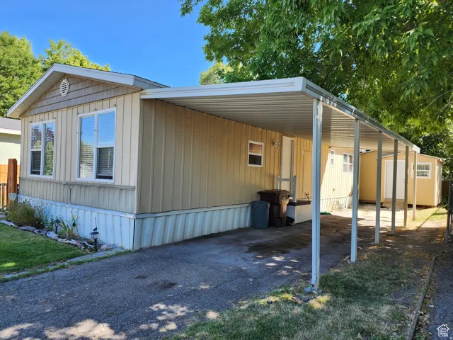 Exterior featuring tan vertical siding, white frame windows, a covered carport, and an exterior storage shed