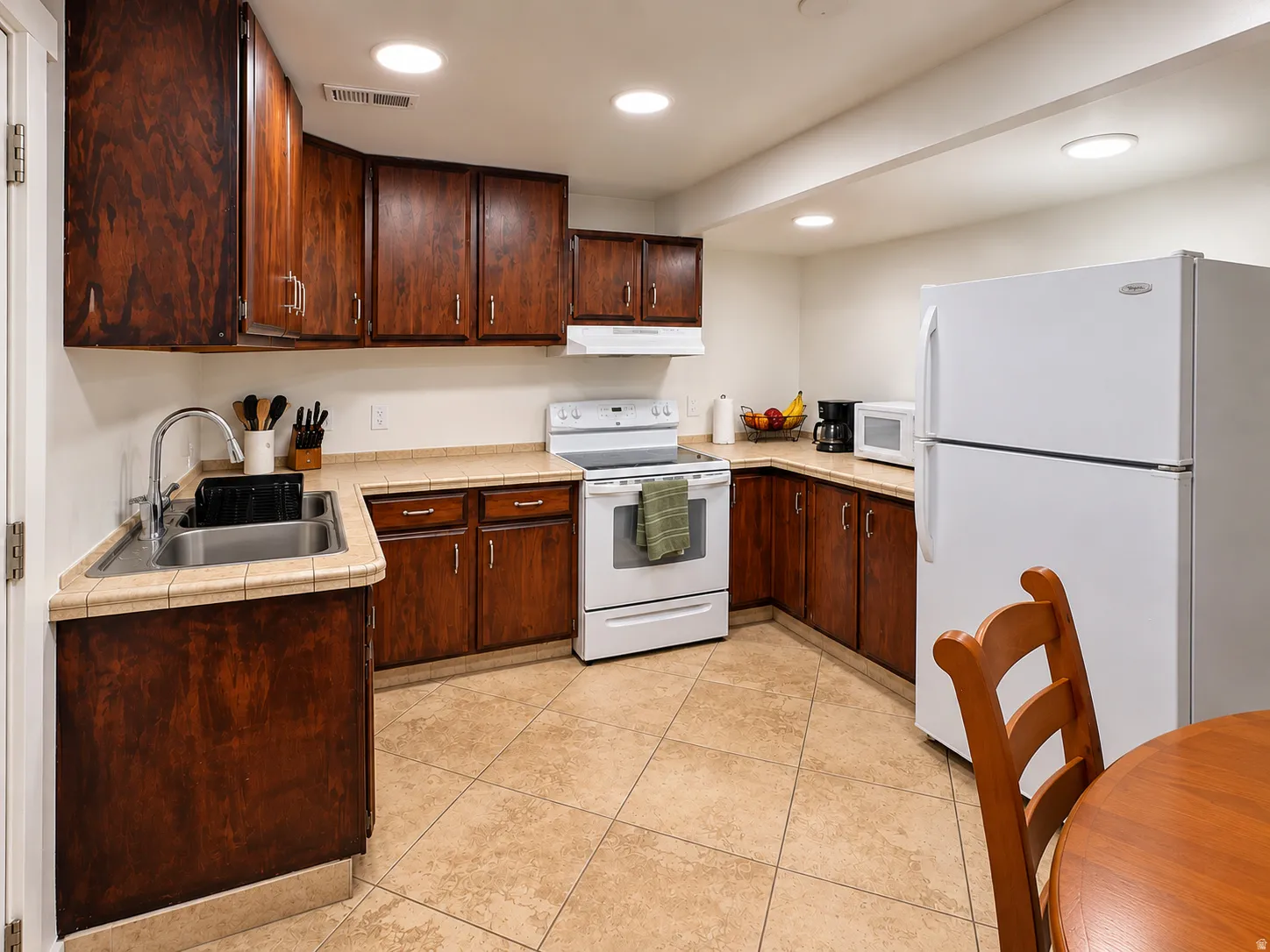 Kitchen featuring wood cabinetry, white appliances, tile flooring, and recessed lighting