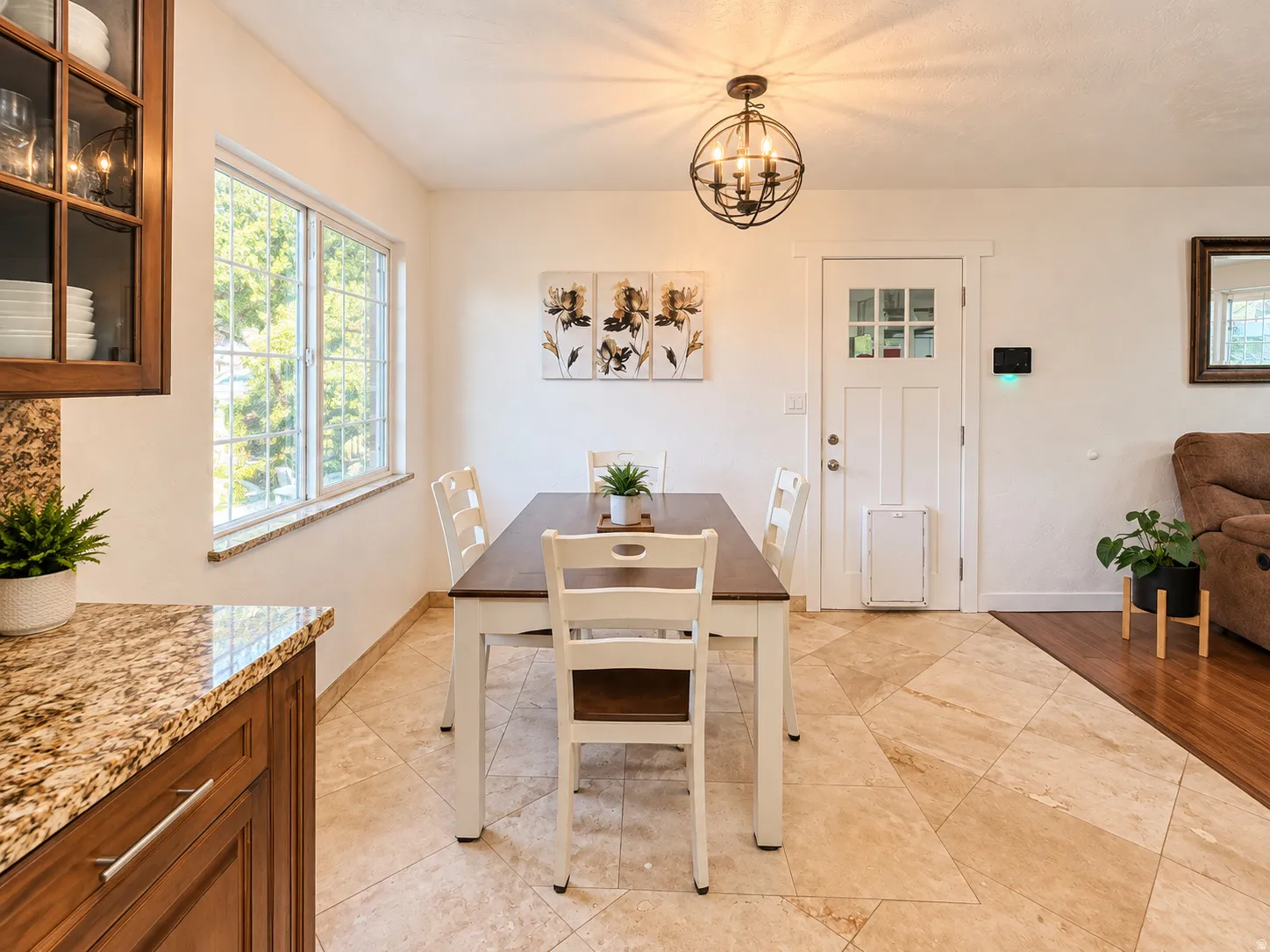 Tile flooring, wood-finish cabinetry, granite countertop, window with gridded panes, and an orb chandelier