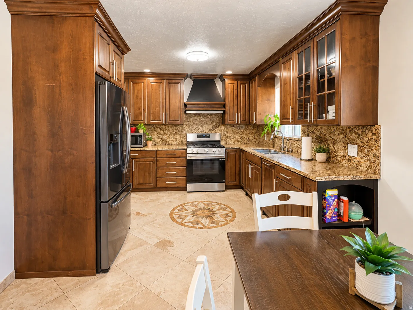 Kitchen featuring wood cabinetry, granite countertops, tile flooring with a decorative inlay, stainless steel appliances, and a black range hood