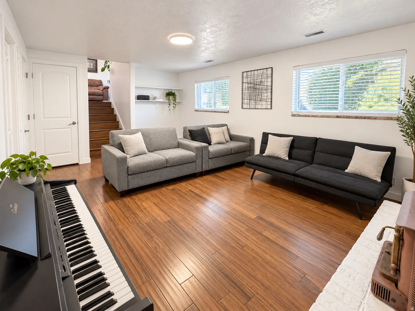 Warm wood-finish flooring throughout, multiple windows with blinds, a white-painted brick hearth, white walls, and built-in shelving