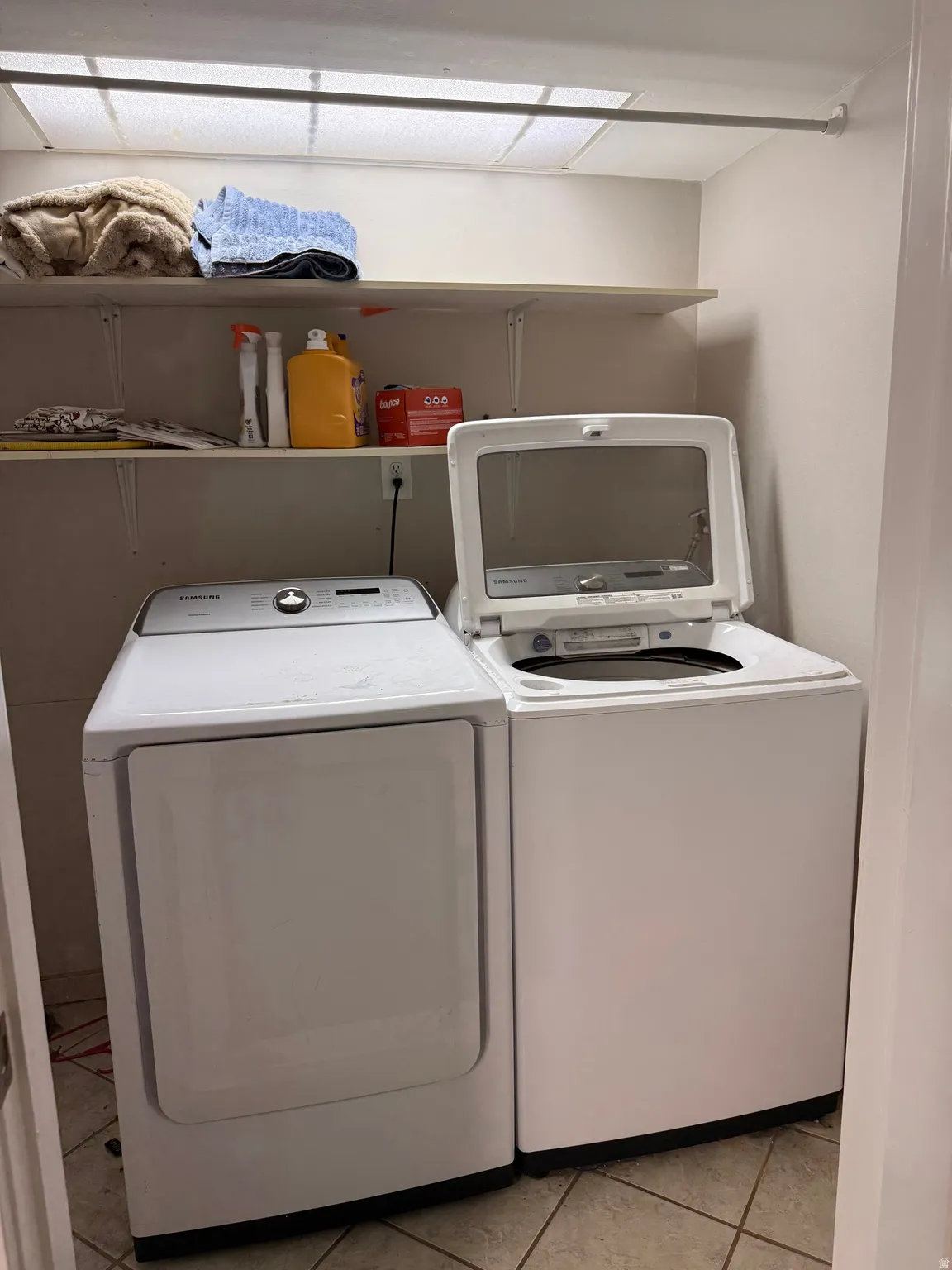 Dedicated laundry area featuring a white top-load washing machine, white front-load dryer, and overhead shelving