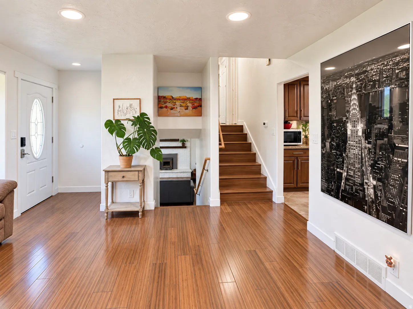 Wood-finish flooring, white paneled entry door with oval glass insert, recessed lighting, wood staircase with white risers, and built-in shelving