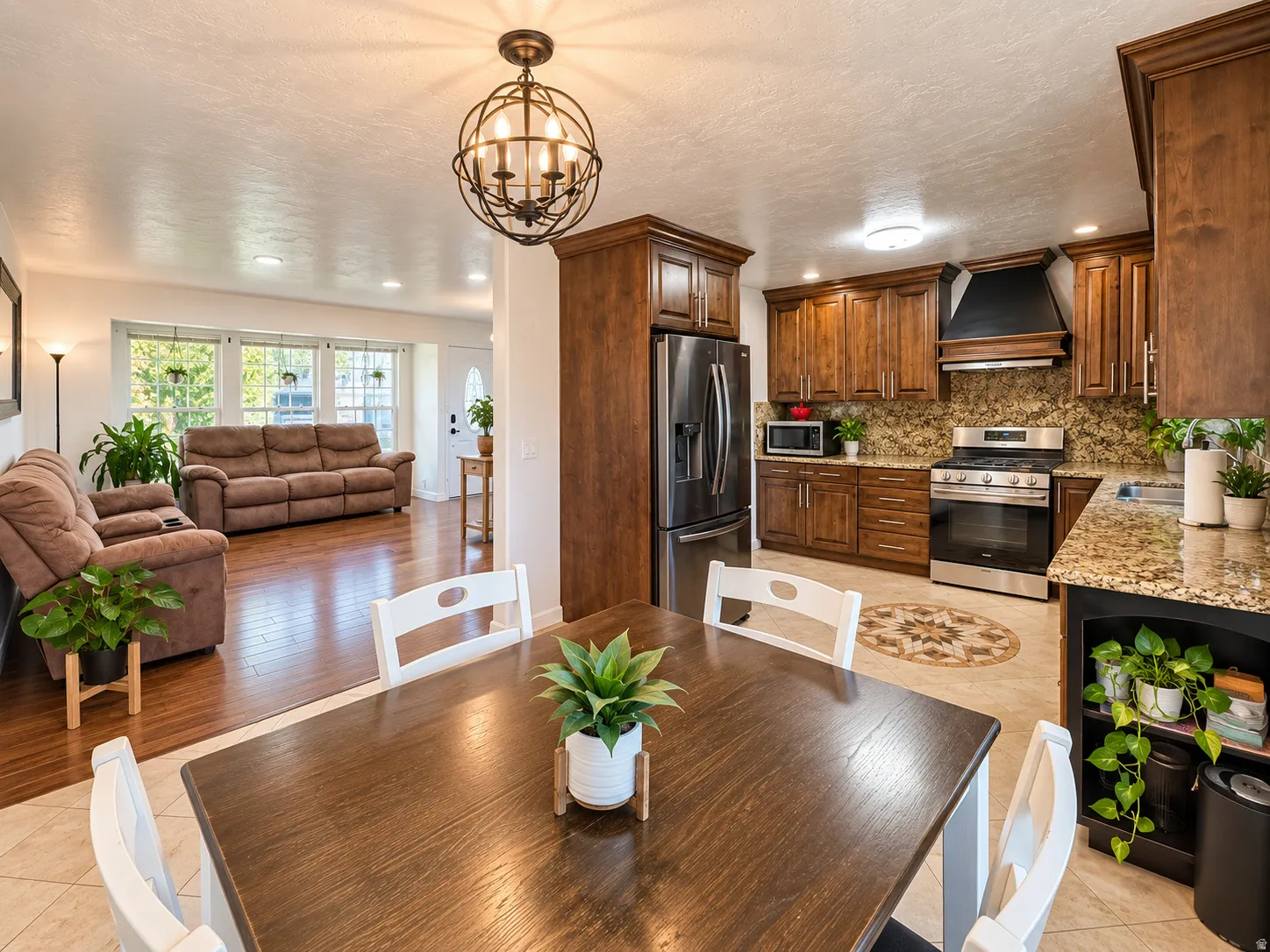 Wood-finish flooring, kitchen featuring stainless steel appliances, wood cabinetry, granite countertops, and an ornate globe chandelier