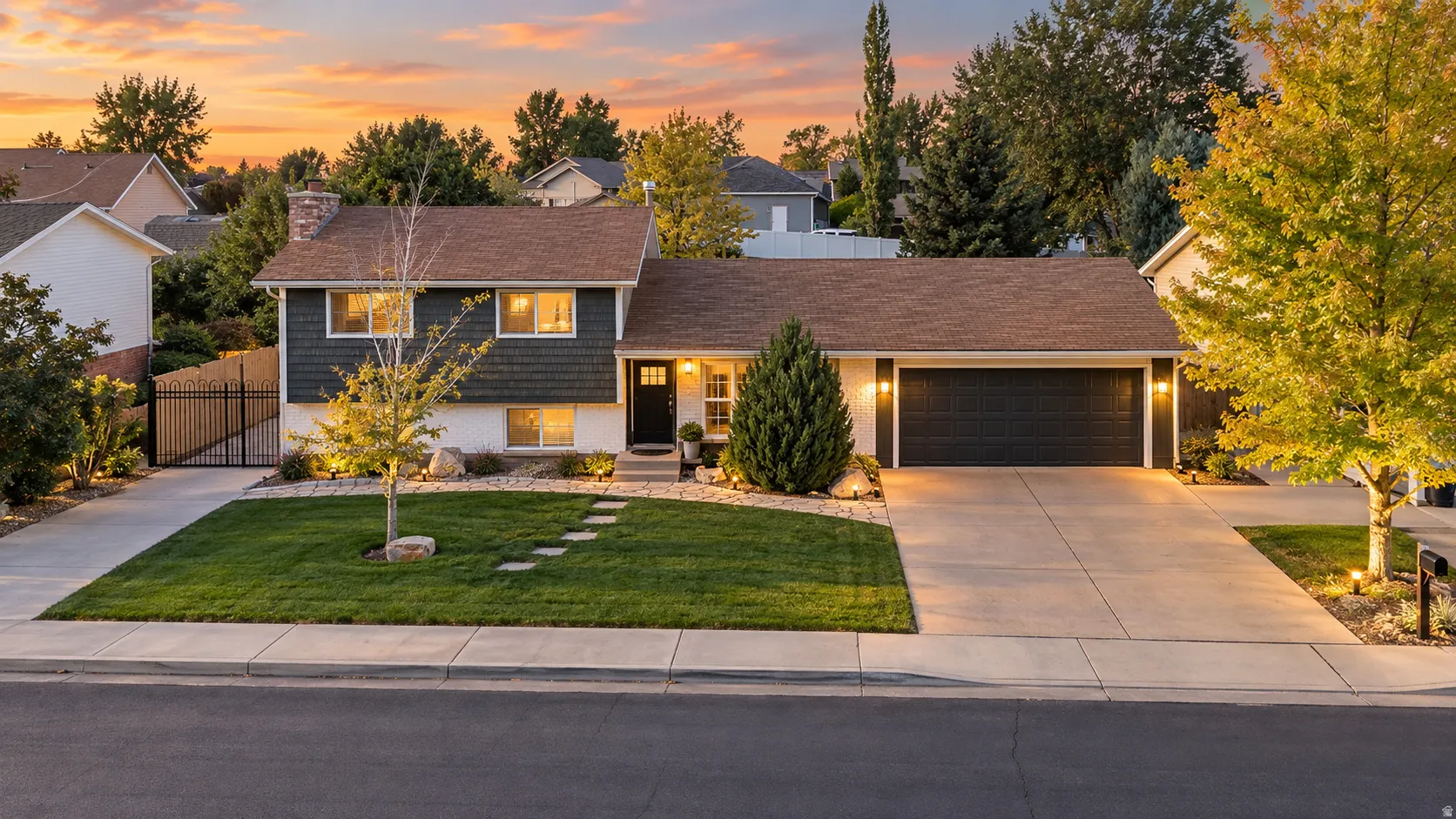 Split-level residence featuring a two-car garage, manicured lawn with stepping stones, and a stone chimney