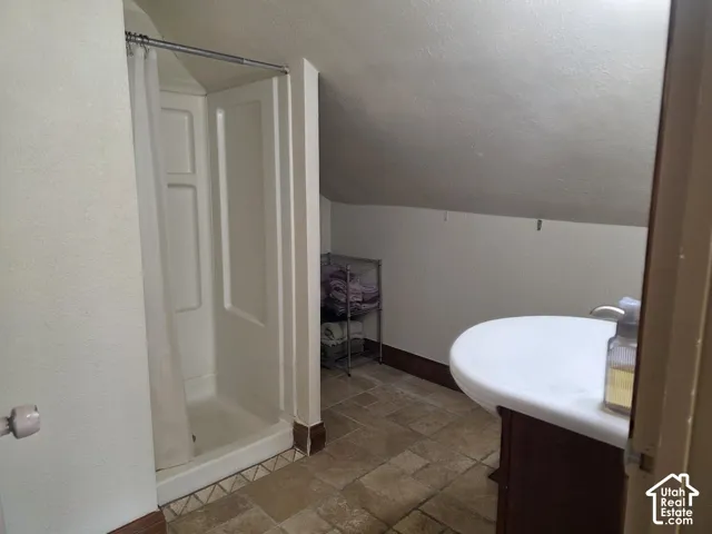Shower enclosure with white surround, pedestal sink with integrated countertop, and tiled flooring