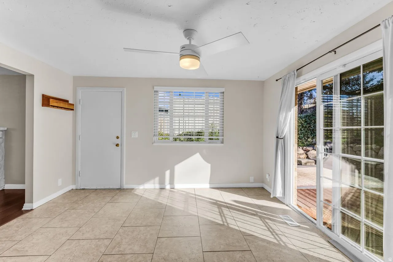 Tiled flooring, white ceiling fan with integrated lighting, sliding glass doors, window with blinds, and a white entry door with brass hardware