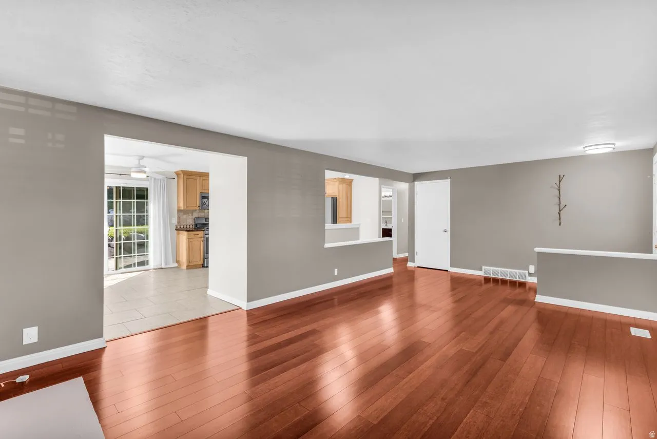 Hardwood flooring, neutral gray wall tones, ceiling-mounted light fixture, sliding glass door, and kitchen with wood-finish cabinetry