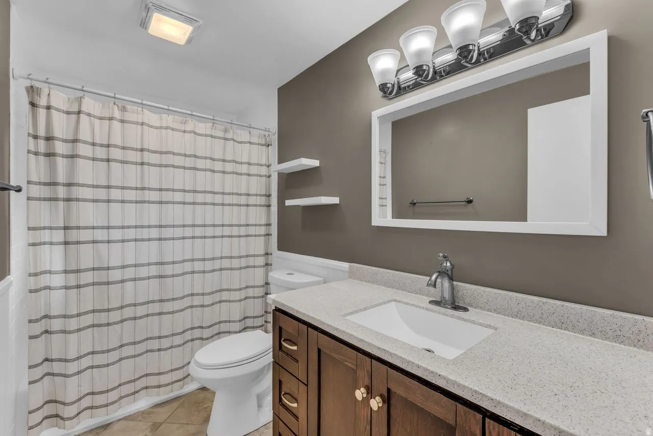 Bathroom featuring a wood-finish vanity with a light-colored countertop, an undermount sink, and a framed mirror with overhead lighting