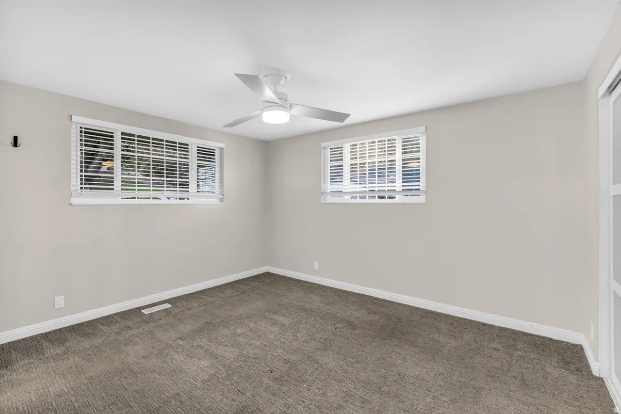 Neutral wall color with two windows, a ceiling fan, and carpeted flooring