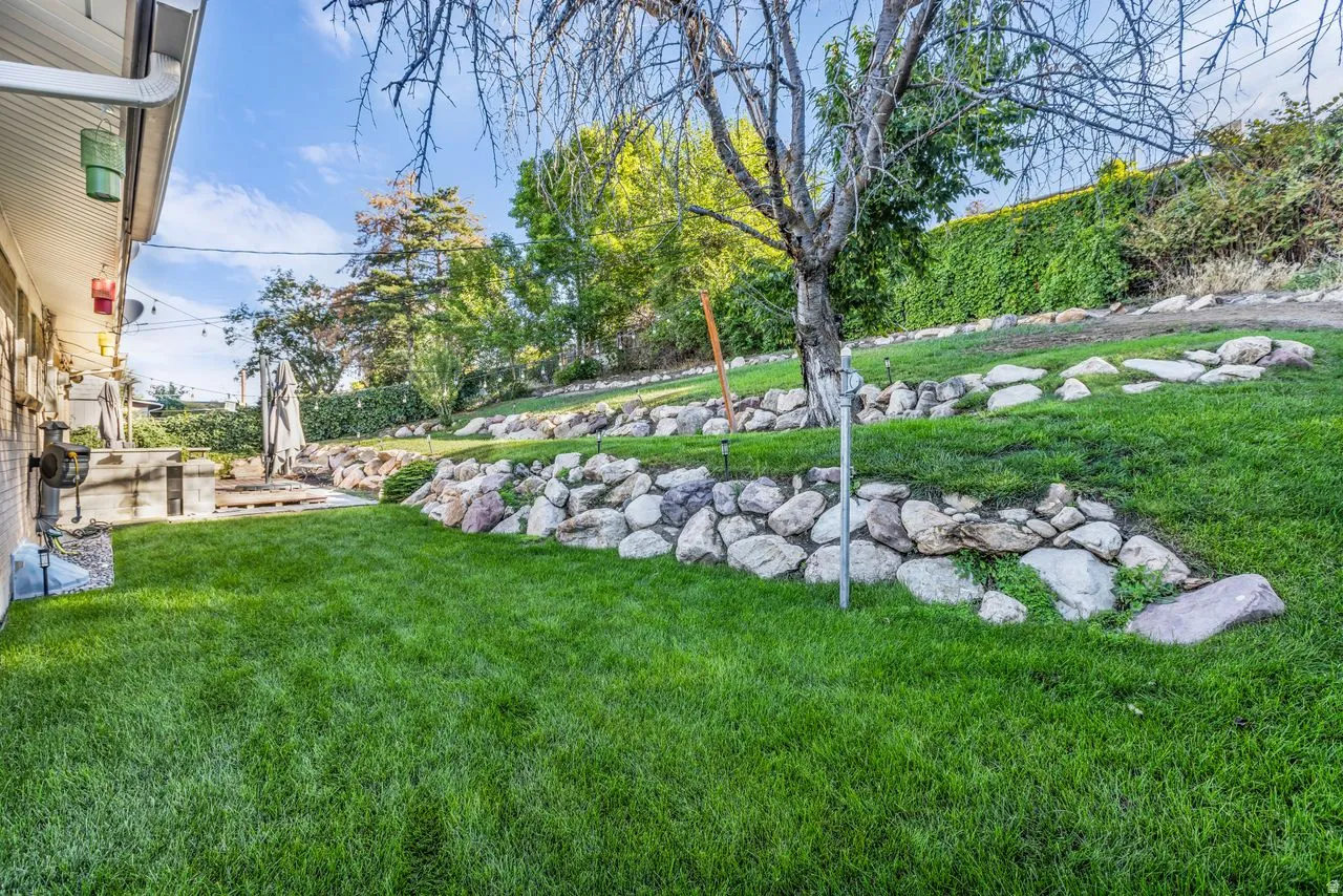 Expansive green lawn, multi-level landscaping with stone retaining walls, and a stone patio area