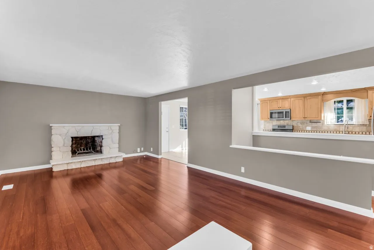 Hardwood-finish flooring throughout, stone fireplace, and a pass-through opening to the kitchen