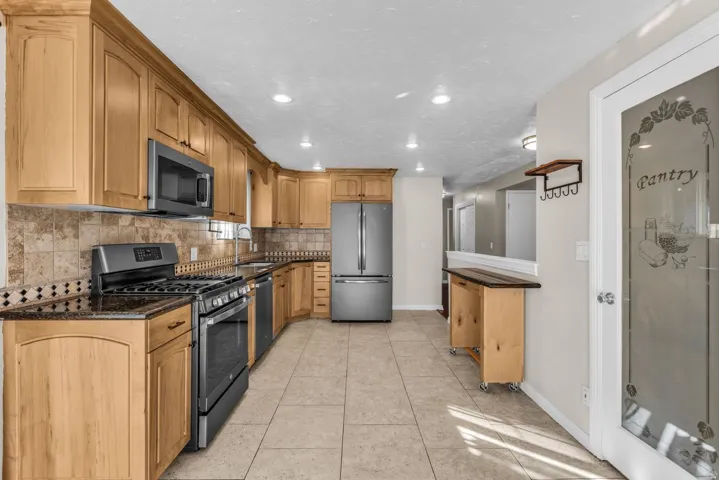 Kitchen featuring light wood cabinetry, dark countertops, a tiled backsplash, and stainless steel appliances