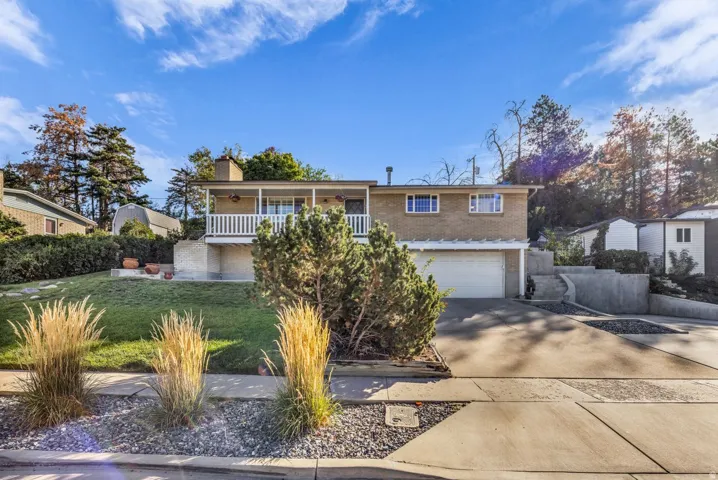 Brick exterior featuring a front balcony with white railing, an attached garage, a concrete driveway, and front landscaping with decorative grasses and gravel