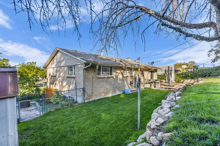 Expansive backyard featuring a manicured lawn, stone retaining wall, and a raised wooden deck