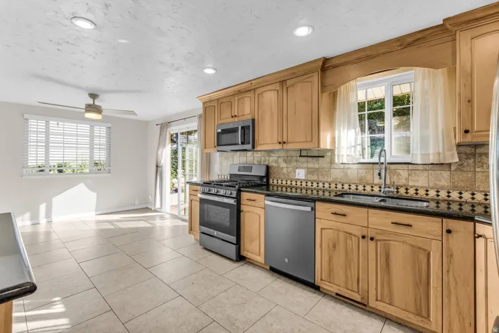 Kitchen featuring wood cabinetry, dark countertops, tile backsplash, and stainless steel appliances