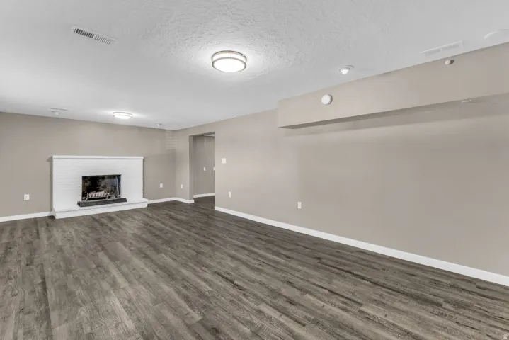Spacious interior with wood-finish flooring, a white brick fireplace, and flush-mount ceiling lights
