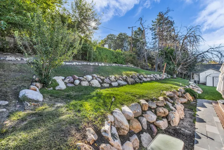Terraced backyard with rock retaining walls, mature trees, and a ground-level patio