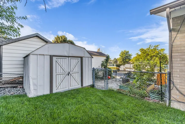 Manicured lawn, metal storage shed with double doors, established garden beds, chain-link fencing, and brick exterior detail