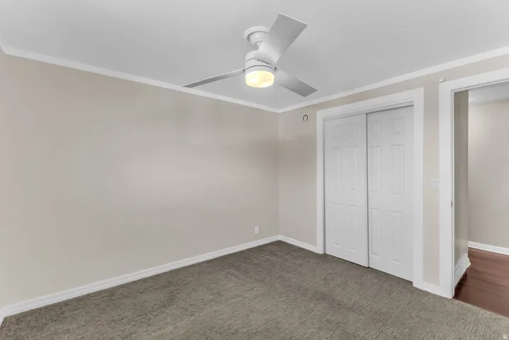 Carpeted room featuring a ceiling fan with integrated lighting, white trim, and bi-fold closet doors