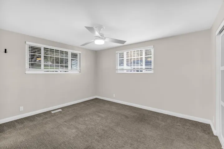 Neutral wall color with two windows, a ceiling fan, and carpeted flooring