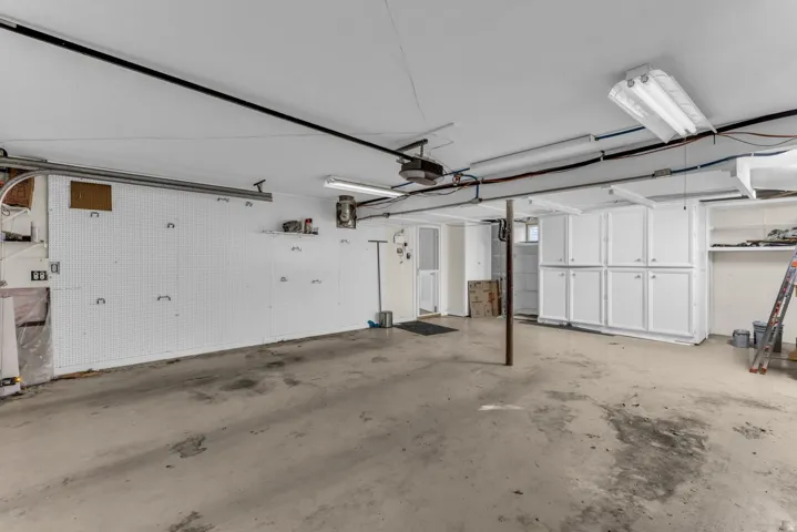 Spacious garage featuring a concrete floor, built-in white cabinetry, and overhead fluorescent lighting