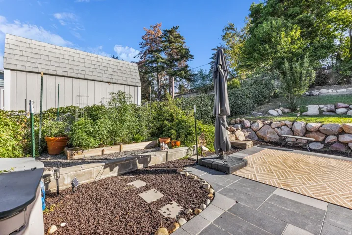 Landscaped backyard featuring a stone retaining wall, paved patio, and raised garden beds