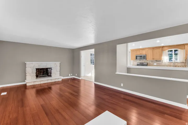 Hardwood-finish flooring throughout, stone fireplace, and a pass-through opening to the kitchen