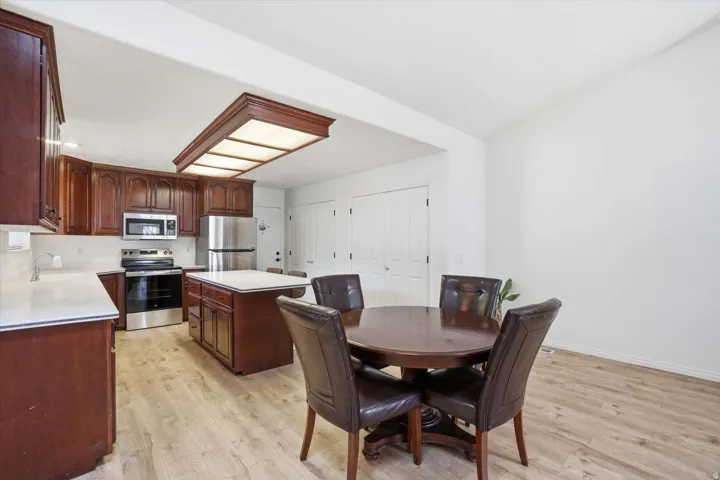 Kitchen and dining area featuring dark wood cabinetry, stainless steel appliances, a center island with a white countertop, and wood-finish flooring