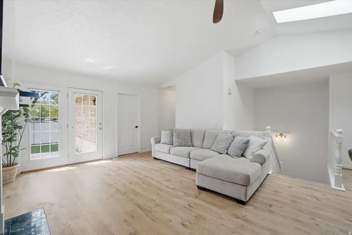 Vaulted ceiling with skylight, wood-finish flooring, white painted walls, and a glass-paneled exterior door