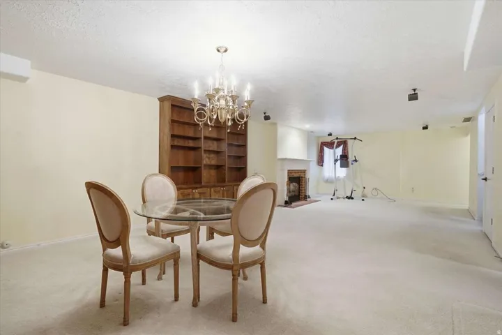 Spacious room featuring a central chandelier, built-in wooden shelving, a fireplace with a white mantel, and light-colored carpeting