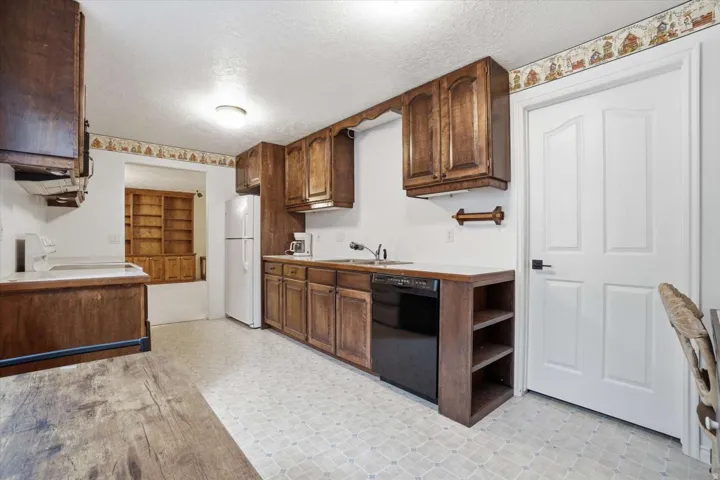 Kitchen featuring wood-finish cabinetry, white countertops, a built-in dishwasher, and patterned flooring