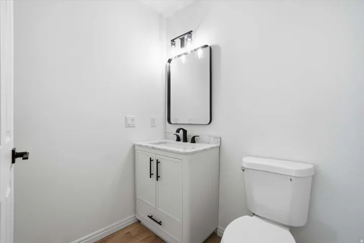 White vanity with black hardware, black-framed mirror, contemporary light fixture, and wood-finish flooring